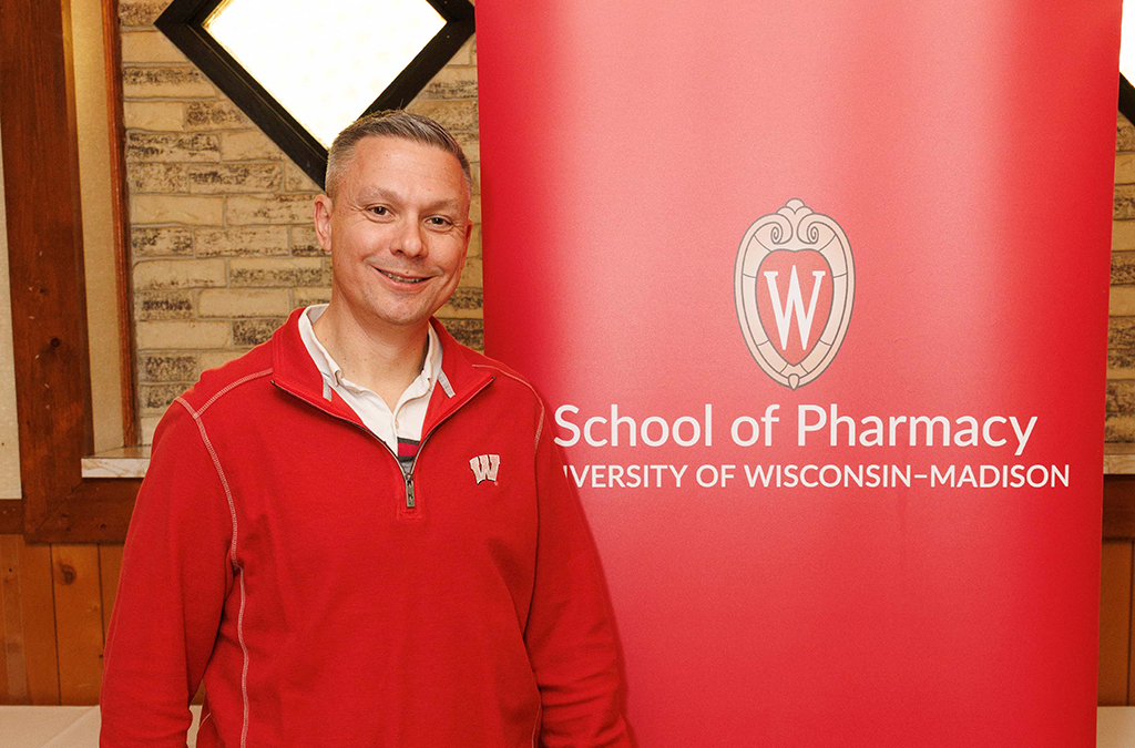 Nick Olson portrait near a red School of Pharmacy banner