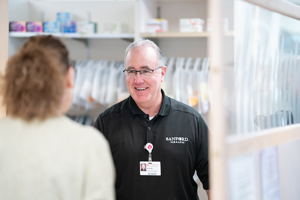 Brian McIlhone in a pharmacy speaking with a woman who is facing away from the camera