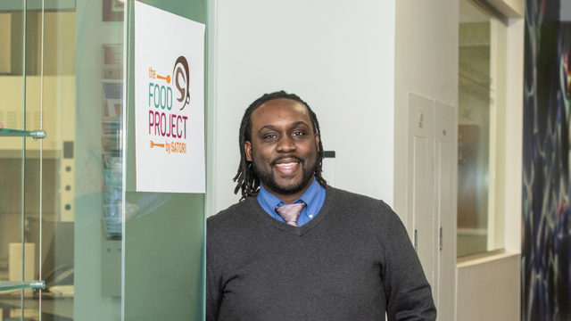 Kwadwo Owusu-Ofori standing by sign reading "The Food Project by Satori"
