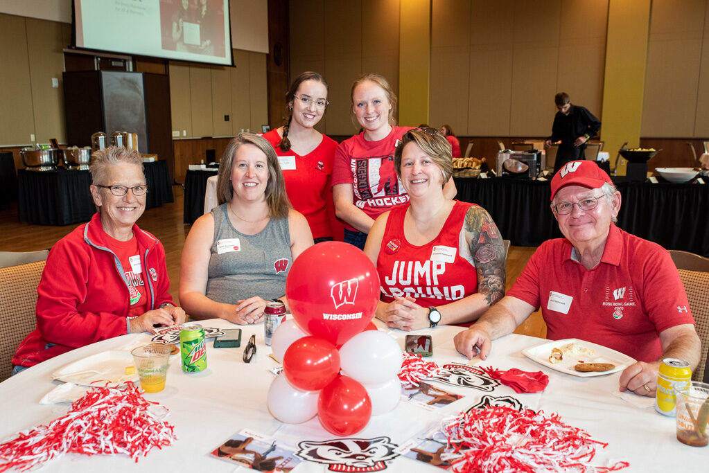 A group of alumni, including Patti, Steve, Mary, and Elizabeth Thornewell, smile and pose with Bucky gear.