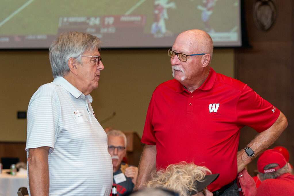 Two older male alumni speak during the viewing party.