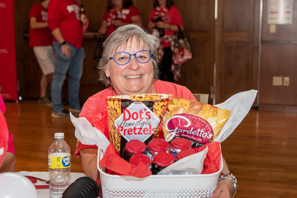 An alum poses with a raffle prize: a basket of snacks.