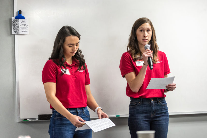 Two women wearing red School of Pharmacy shirts with one holding a microphone