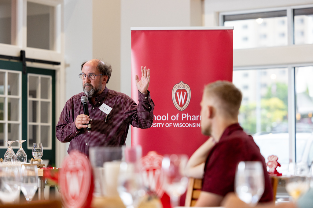 Jay Ford speaks at a microphone in front of a School of Pharmacy banner