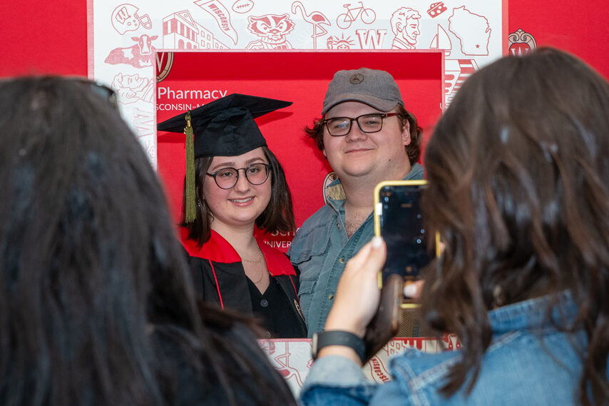 PharmTox student holding frame prop in front of red backdrop