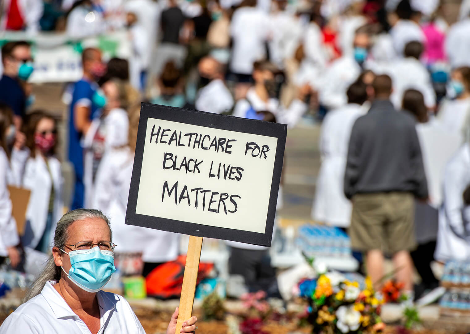 Woman in white coat holding up sign reading "Healthcare for Black Lives Matters"