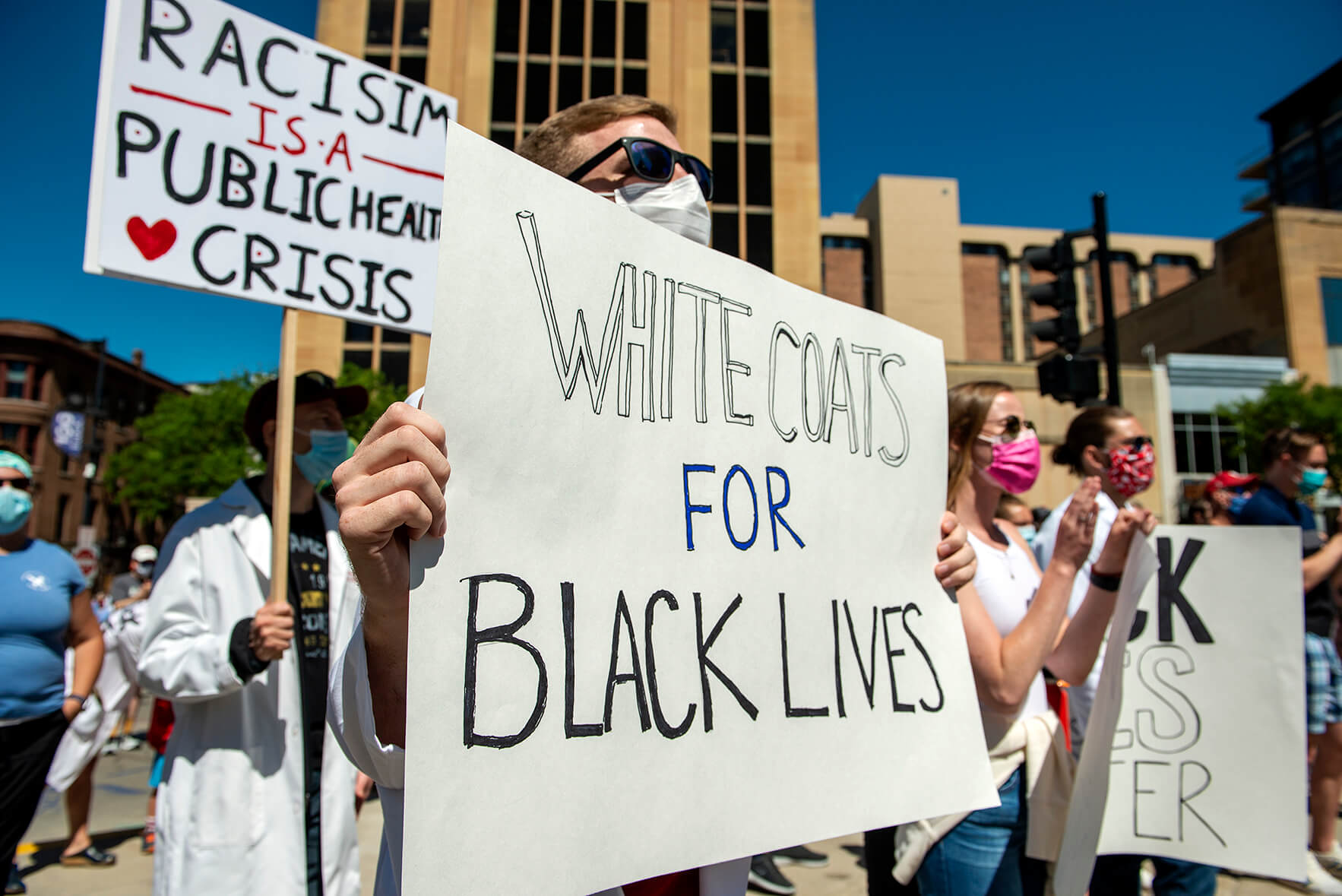 Close up on student holding sign reading "White coats for Black Lives"