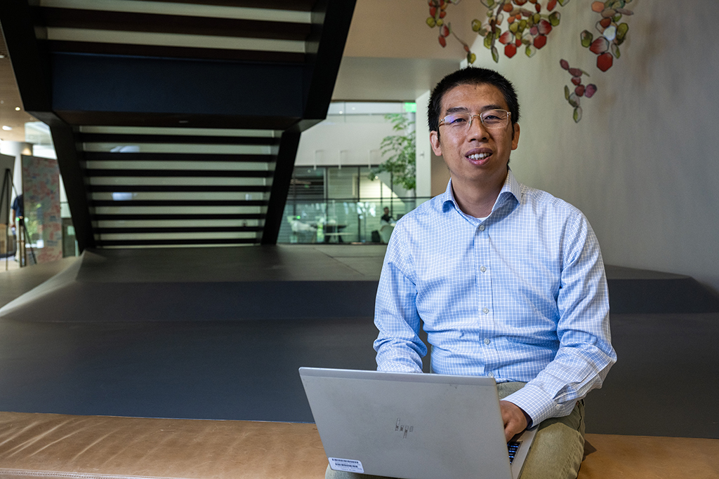 Wei Zhang works on his computer beneath stairs and smiles