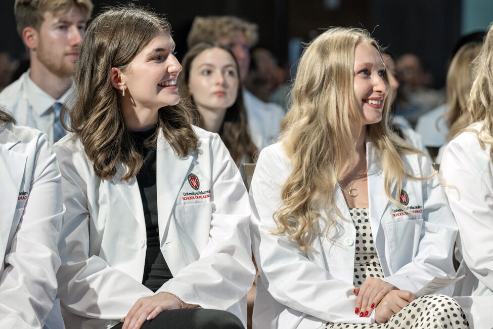 PharmD students smile in their seats wearing white coats