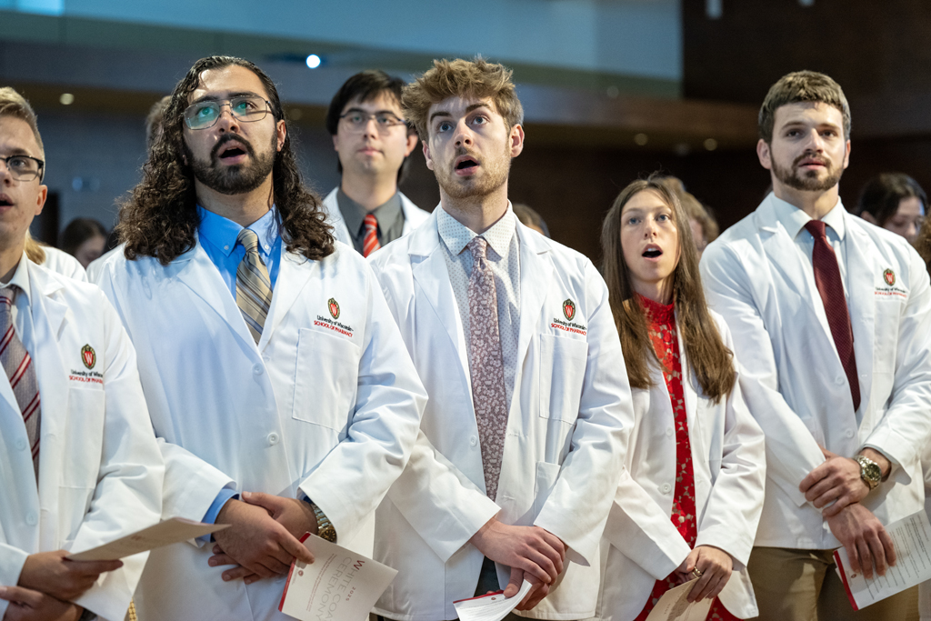 PharmD students in white coats stand and speak