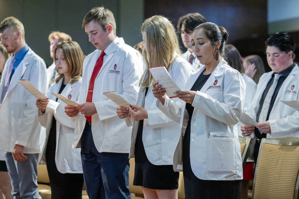 PharmD students in white coats stand and read from their programs
