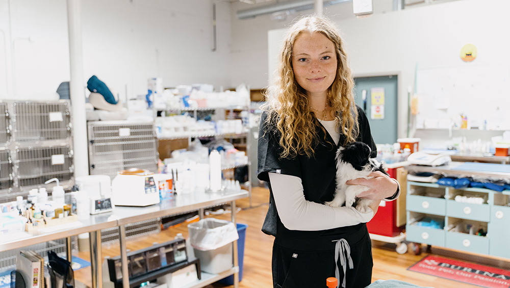 Sydney Wiese in scrubs, holding a small dog.
