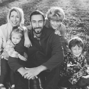 Alum Nate Johnson sits in the grass with his wife and three children.