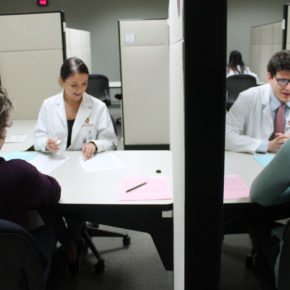 communications lab with students wearing white coats speaking to patients