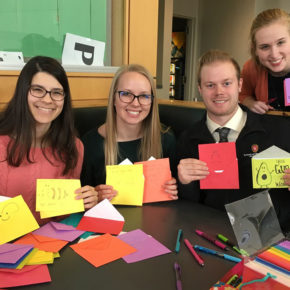 Lindsey Skubitz, Kelsey Eickstaedt, Bernard Brooks, and Olivia Merillat holding up colorful valentine's cards with paper and markers in front of them.