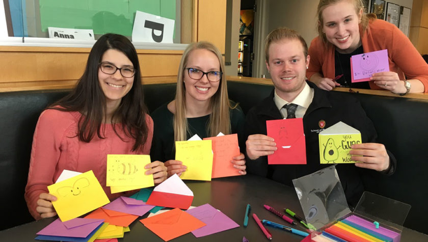 Lindsey Skubitz, Kelsey Eickstaedt, Bernard Brooks, and Olivia Merillat holding up colorful valentine's cards with paper and markers in front of them.