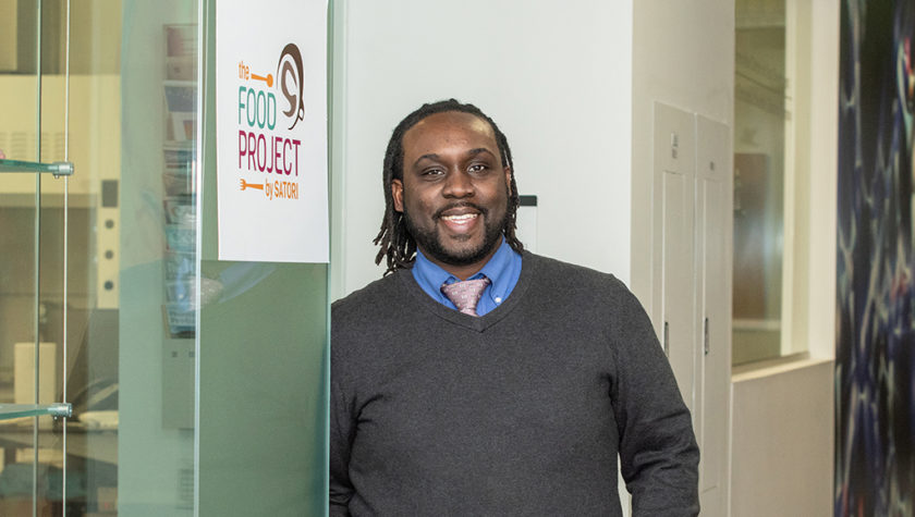 Kwadwo Owusu-Ofori standing by sign reading "The Food Project by Satori"