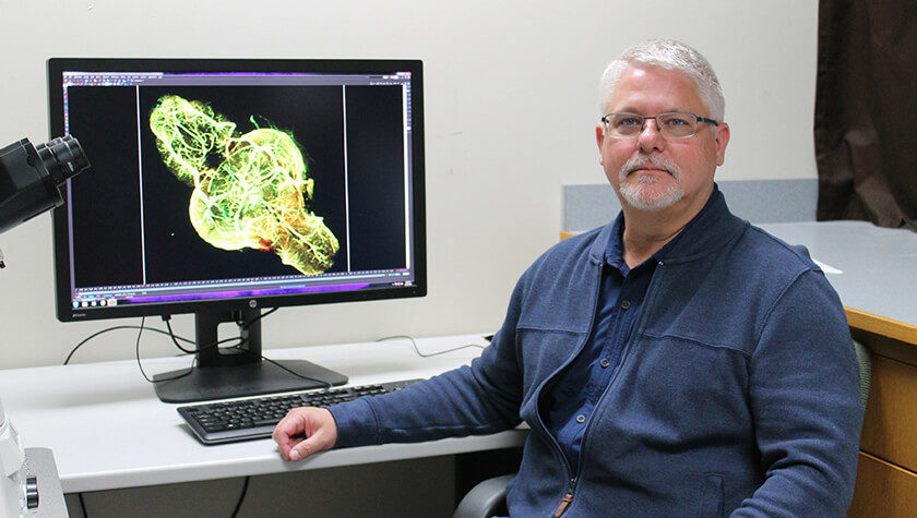 Michael Taylor at his desk with 3D rendered image on computer