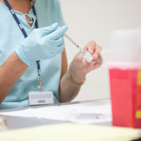 Nurse wearing glove extracting liquid from vial with syringe