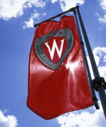 A "W" crest banner flies on Bascom Hill against blue sky and puffy clouds during spring. ©UW-Madison University Communications Photo by: Jeff Miller