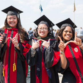 PharmD graduates Lorewell Buaya, Kathy Chao, and Silvya Velez Pache pose together with W hand gestures at Memorial Union Terrace following the 2022 Hooding Ceremony.