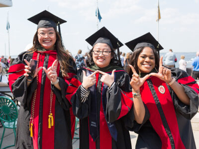 PharmD graduates Lorewell Buaya, Kathy Chao, and Silvya Velez Pache pose together with W hand gestures at Memorial Union Terrace following the 2022 Hooding Ceremony.