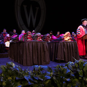 Dean Steve Swanson onstage, speaking at a podium in graduation robes