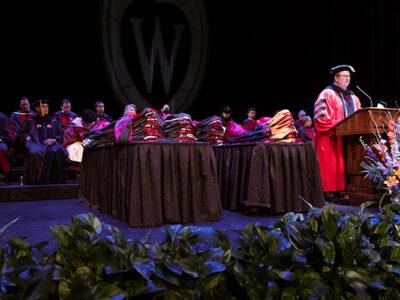 Dean Steve Swanson onstage, speaking at a podium in graduation robes