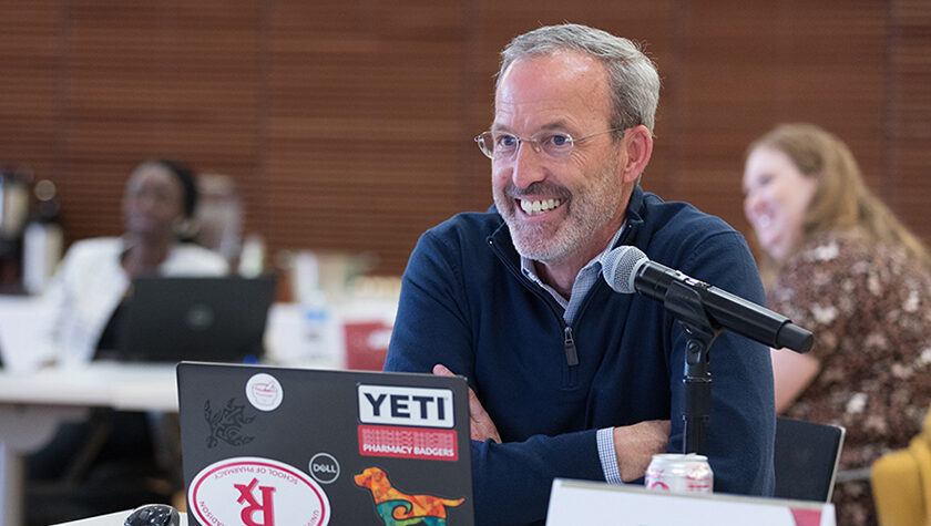 Dave Mott sitting at a table with a laptop and a diet coke with a microphone close to him