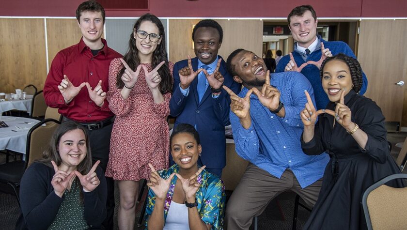 Students together in a large dining room, using their hands to form a "W" for the camera