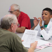 A young boy smiles and looks on as an older attendee reviews a worksheet