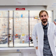 Cody Wenthur holding up a molecule model in his lab and smiling