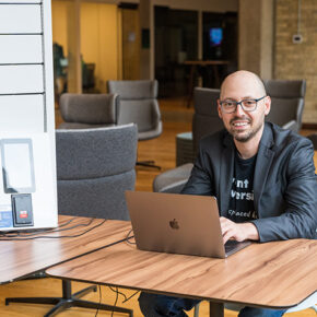 Alex Yampolsky smiles from behind a laptop, next to a white MedServe cabinet