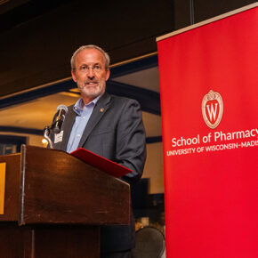 Dave Mott speaks at a lectern in front of a red School of Pharmacy banner