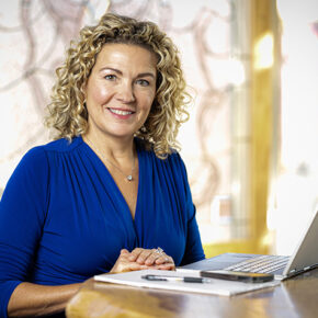 Lani Bertrand smiles while seated at a table in front of a laptop.