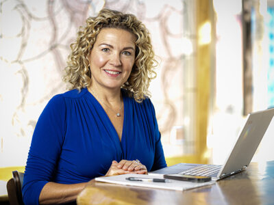 Lani Bertrand smiles while seated at a table in front of a laptop.