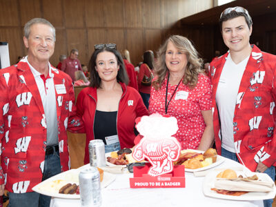 Denise Kachel with her husband, son, and daughter, all dressed in Badger red. The two men wear sport coats with Bucky badger and Ws on them.