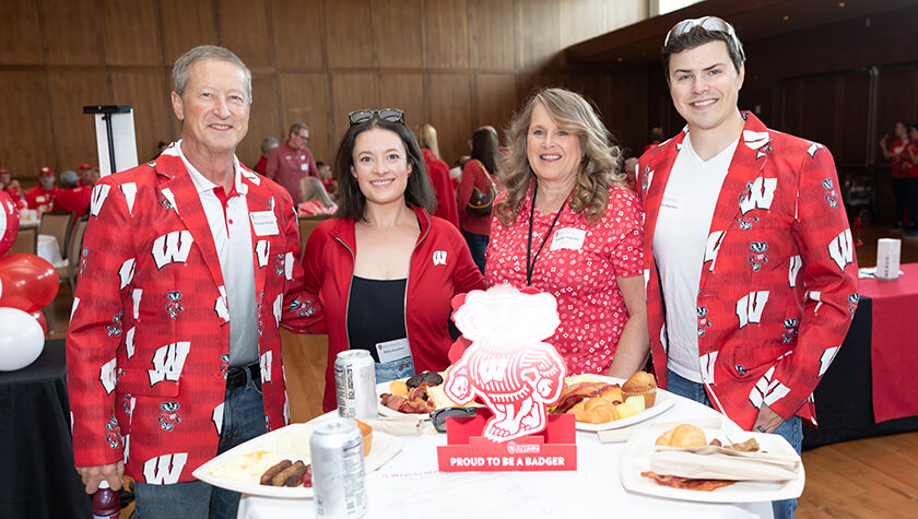 Denise Kachel with her husband, son, and daughter, all dressed in Badger red. The two men wear sport coats with Bucky badger and Ws on them.