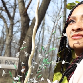 Thi Le, wearing leaves in her hair, looks back over her shoulder next to a sign reading "murderers' row."