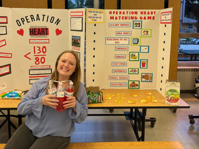 Kelsie Tingle poses in front of a poster board about heart health.