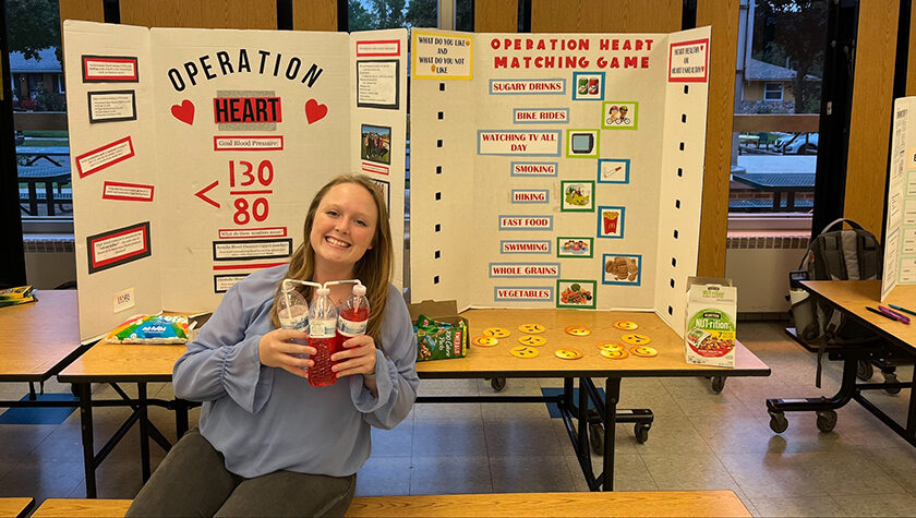 Kelsie Tingle poses in front of a poster board about heart health.