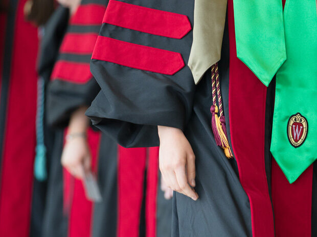 A colorful collection of graduation robes, tassels, and stoles of students lined up waiting to walk into the School of Pharmacy Hooding Ceremony
