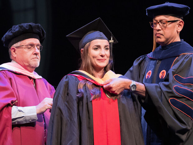 Professors Mel de Villiers and Arash Bashirullah fasten a graduate student's hood at the Hooding Ceremony