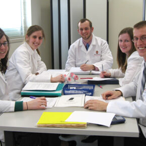 Students in white coats smile at the camera