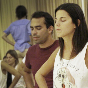 A small group of people sitting with eyes closed and hands on hips