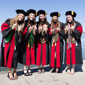 A group of graduates in robes hold up W hands