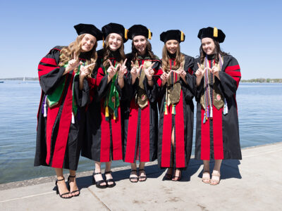 A group of graduates in robes hold up W hands