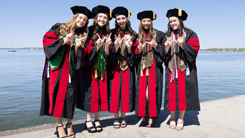 A group of graduates in robes hold up W hands