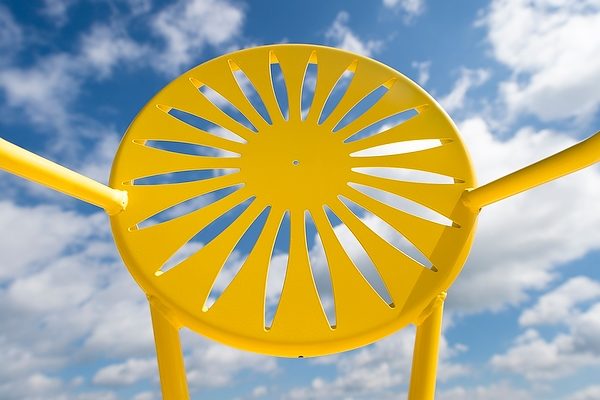 A yellow Memorial Union Terrace chair is pictured against a sunny blue sky at UW-Madison.. The chair is known for its iconic sunburst design. (Photo by Jeff Miller/UW-Madison)