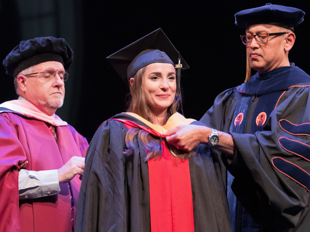 Two professors fasten a graduate student's hood